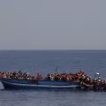 232 in Seenot geratene Menschen mit Rettungswesten auf einem Holzboot im Mittelmeer