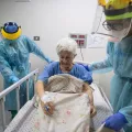 Alte Frau wird von zwei Pflegern in Schutzkleidung betreut