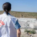Eine Person von hinten fotografiert, mit einer Ärzte ohne Grenzen Weste die auf ein entferntes Camp schaut