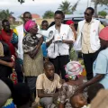 Eine Community Health Mitarbeiterin klärt mit einem Megaphon auf dem Buterere-Markt in Bujumbura über Cholera auf. Um sie herum sind mehrere Mitarbeiter sowie weitere Personen versammelt und hören zu.