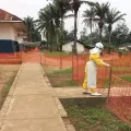 Person in Schutzanzug vor Zaun vor einem Ebolabehandlungszentrum in der DR Kongo.