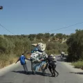 Geflüchtete laufen auf einer Straße, in ihrer Mitte ein Wagen mit Ihrem Hab und Gut.