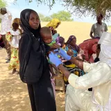 Mitarbeitender untersucht ein Kleinkind, das von einer Frau im Arm gehalten wird.