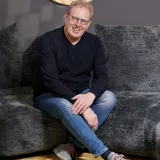 Uli Held sitzt auf dem Sofa und schaut in die Kamera.